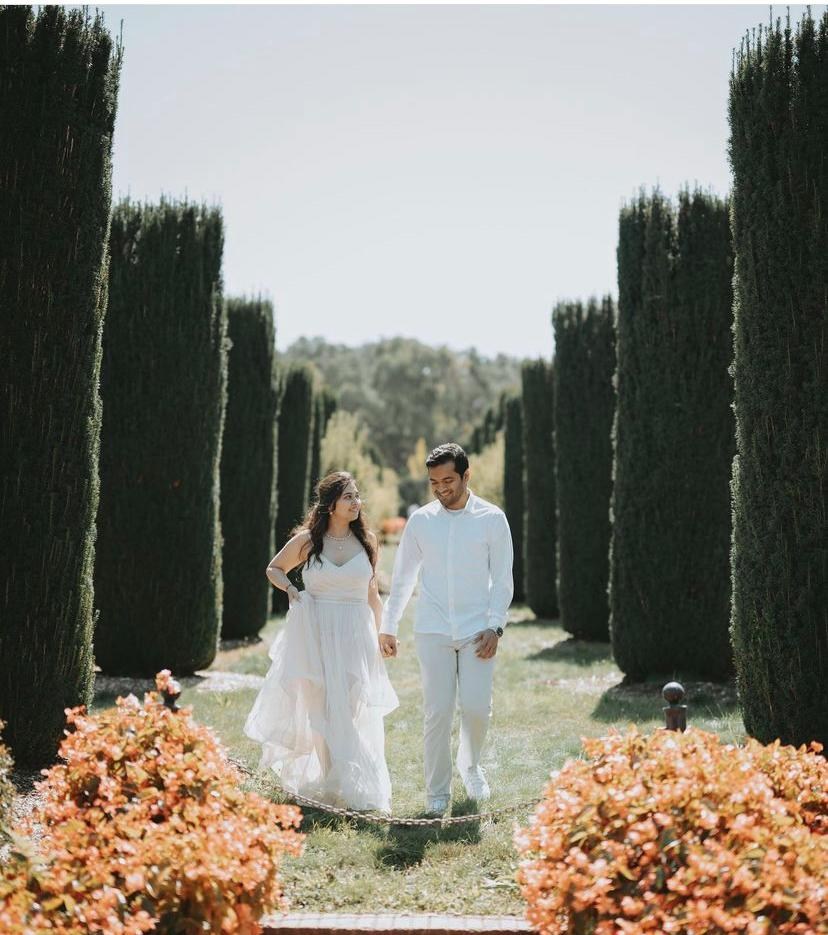 Karan and Prachi, dressed in white, walking hand in hand through a garden
