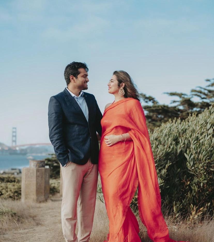 Karan and Prachi smiling at each other near the Golden Gate Bridge, Prachi in an orange saree